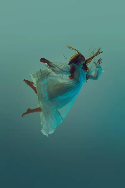 Woman in stunning dress, gracefully suspend in water, conveys sense of fluidity and grace against serene aqua background. Concept of underwater fantasy, freedom and weightlessness, mystery and depth.