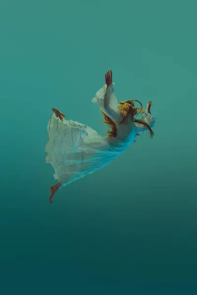Young woman in flowing dress exudes calm and peace elegantly, gracefully floating against serene aqua background. Concept of underwater fantasy, freedom and weightlessness, mystery and depth. Ad