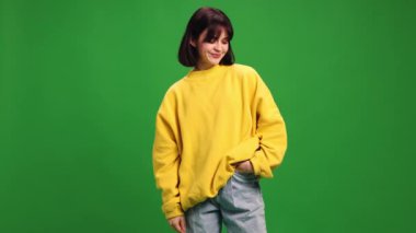 Kısa saçlı, kısa saçlı, sarı kazaklı genç bir kadın ve canlı yeşil stüdyo arka planında kameraya bakıyor. İnsan duyguları kavramı, moda, güzellik, tarz.