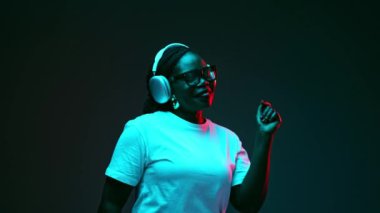 Rahatlamış Afro-Amerikalı kadın kulaklıkla müzik dinliyor ve gradyan stüdyo arka planına karşı kırmızı ışıkta şarkı söylüyor. İnsani duygular, güzellik ve moda kavramı, tarz,