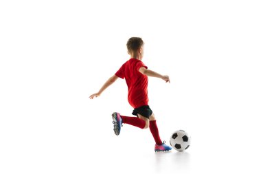 Sportif küçük çocuk, beyaz stüdyo arka planına karşı mükemmel bir atış yapmak için topa vuruyor. Küçük futbolcu mükemmel pas veriyor. Profesyonel spor kavramı, şampiyonluk, gençlik ligi, hobi