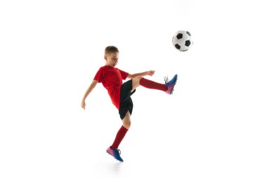 Beyazların arka planında futbol topuyla uçan tekme atan küçük sporcu çocuk. Dinamik bir portre. Profesyonel spor, şampiyonluk, gençlik ligi, hobi. Ad