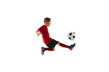 Sportif bir çocuğun dinamik portresi, kırmızı üniformalı bir çocuk oynuyor, futbol antrenmanlarını beyazların arka planında yapıyor. Profesyonel spor, şampiyonluk, gençlik ligi, hobi. Ad