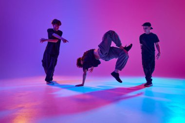 Enerjik gençlerin üçlüsü, yetenekli break dansçıların hareketli neon ışıkları altında canlı gradyan arka planda dans etmesi. Spor ve hobi kavramı, müzik, moda ve sanat, hareket. Ad