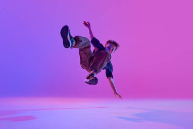 Yetenekli bir genç çocuk, sokak dansçısı, parlak arka plana karşı karışık neon ışıkta numaralar yapıyor. Spor ve hobi kavramı, müzik, moda ve sanat, hareket. Ad