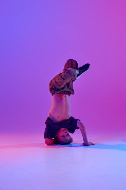 Breakdance yapan genç erkek solo sanatçı, karışık neon ışıkta hareketli hip-hop dansı canlı gradyan arka planda. Spor ve hobi kavramı, müzik, moda ve sanat, hareket. Ad