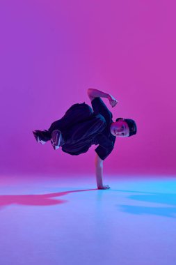 Yüksek enerjili dans. Genç bir çocuk, karışık neon ışıklarıyla karışık bir dans hareketini canlı arkaplana karşı gerçekleştiriyor. Spor ve hobi kavramı, müzik, moda ve sanat, hareket. Ad