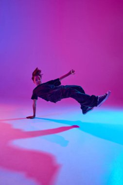 Genç sokak dansçısı, dinamik pozda, siyahlar içinde, neon ışıkları altında canlı bir arka planda. Spor ve hobi kavramı, müzik, moda ve sanat, hareket. Ad