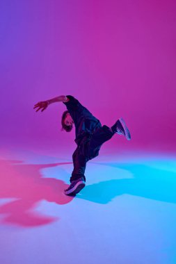 Genç sokak dansçısı, dinamik pozda, siyahlar içinde, neon ışıkları altında canlı bir arka planda. Spor ve hobi kavramı, müzik, moda ve sanat, hareket. Ad
