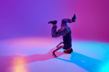 Şık giyinmiş genç bir dansçı, kafası üzerinde dönen bir adam karışık neon ışıklarıyla hareketli bir arka plan. Spor ve hobi kavramı, müzik, moda ve sanat, hareket. Ad