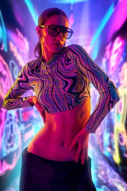 Canlı bir sokak tarzı. Eşsiz bir bluz ve modaya uygun gözlük takan renkli neon duvar yazıları olan bir kadının portresi. Gençlik kavramı, güzellik, moda ve tarz, modern yaşam tarzı. Ad