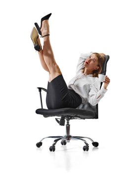 Beyaz arka planda kahve içerken ofis koltuğunda oturan ve bacaklarını kaldıran şık takım elbiseli genç bir kadın hayal ediyorum. İş, iş ve öğrenim kavramı, hobi, serbest çalışma. Ad