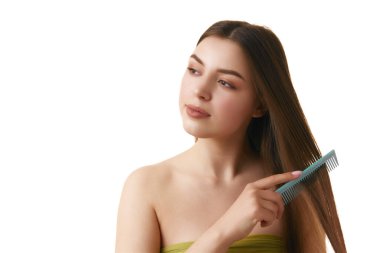 Çıplak omuzlu genç bir kadın beyaz stüdyo arka planında ipeksi düz saçlarını tarıyor. Uzayı kopyala Saç tedavisi, hijyen, spa prosedürleri, sağlık. Ad