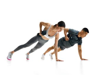 Beyaz stüdyo arka planında halterlerle tahta sıra egzersizi yapan sağlıklı erkek ve kadının dinamik görüntüsü. Spor, sağlıklı yaşam tarzı, takım çalışması, motivasyon. Ad