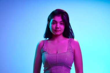 Çekici genç Hintli kız, 20 'li yaşlarda, hafif gülüşlü kameraya bakıyor pembe neon ışıkta, eğimli mavi arka planda. İnsan duyguları, güzellik ve moda kavramı, gençlik. Ad