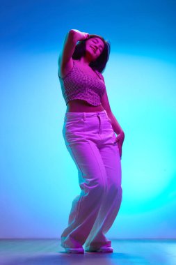 Genç esmer kızılderili kızın pembe neon ışıkta hareket halindeki neon dansının gradyan mavi arka planda tam boy portresi. İnsan duyguları, güzellik ve moda kavramı, gençlik. Ad