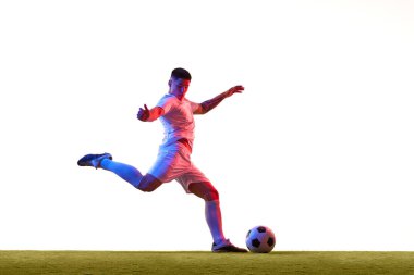 Yeşil şortlu ve beyaz formalı futbolcu, yeşil çimlerin üzerinde beyaz stüdyo arka planına karşı neon ışığında yakalandı. Profesyonel spor, rekabet, turnuva, eylem kavramı.