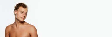 Pankart. Genç, atletik gömleksiz bir adam, beyaz arka plana hafifçe uzak duruyor. Metin eklemek için negatif alanı var. Erkek sağlığı, güzellik ve kendine bakım, gençlik, vücut ve cilt bakımı kavramı.