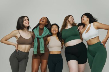 Her biri modaya uygun atletik giysiler giyen, mutlu gülümseyen çeşitli kadınlar vücut çeşitliliğini ve kendini beğenmişliği vurguluyor. Güzellik ve moda kavramı, destek, birlik, sağlık, vücut pozitifliği. Ad