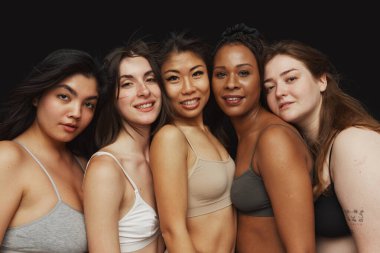 Her birinin farklı vücut şekilleri ve etnik kökenleri olan genç kadınların grup portresi siyah stüdyo geçmişine yakın bir şekilde sarılıyor. Güzellik ve moda kavramı, destek, birlik, sağlık, vücut pozitifliği..