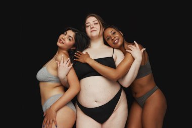 Güzel, kendine güvenen kadınlar her biri farklı vücut şekillerine sahip ve siyah stüdyo geçmişine karşı iç çamaşırı giyen kadınlar. Güzellik ve moda kavramı, destek, birlik, refah, çeşitlilik.
