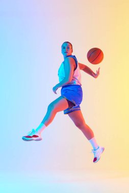 Mavi basketbol kıyafetli atletik bir kadın, neon ışıkta stüdyonun arka planına karşı oynamaya hazır. Profesyonel spor, şampiyonluk, turnuva, hobi ve eğlence kavramı. Ad