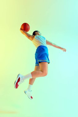 Düşük açılı basketbol oyuncusu, neon ışıkta stüdyonun arka planına karşı mükemmel bir gol atmak için hareket ediyor. Profesyonel spor konsepti, şampiyonluk, turnuva, eğlence. Ad