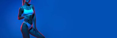 Pankart. İç çamaşırlarıyla poz veren güzel bir kadın mükemmel vücut kıvrımlarını neon ışıklarıyla gradyan mavi arka planda gösterir. Güzellik ve moda kavramı, kadın sağlığı, anti-selülit, diyet