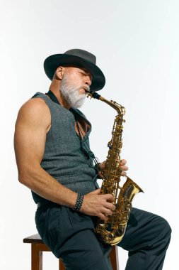 Kolsuz gri yelekli, siyah şapkalı, caz çalan saksafonlu beyaz stüdyo arka planına karşı altın saksafonlu adam. Müzik anlayışı, festivaller, çağdaş sanat, hobi, yaratıcılık. Ad
