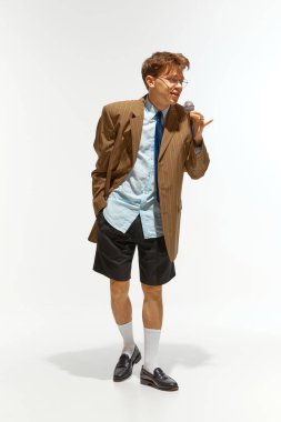 Genç adam büyük beden giyinmiş, beyaz stüdyo arka planında mikrofonla şarkı söylüyor. Müzik anlayışı, festivaller, çağdaş sanat, hobi, yaratıcılık. Ad