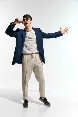 Sanatçı, gündelik giyinmiş, güneş gözlüklü, beyaz stüdyo arka planında mikrofonla şarkı söyleyen bir vokalist. Müzik anlayışı, festivaller, çağdaş sanat, hobi, yaratıcılık. Ad