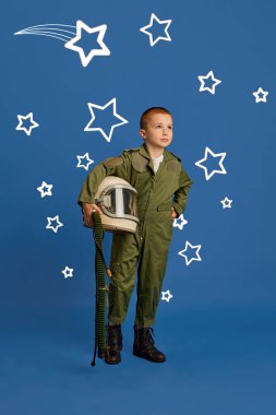 Astronot kostümü giymiş genç bir çocuğun portresi mavi stüdyo arka planında yıldızları ve galaksileri keşfetmeyi hayal ediyor. Çocukların hayalleri, gelecekteki kariyerleri, meslekleri, oyunları, fantezileri. Ad