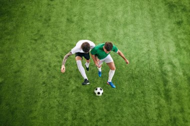 Hava görüntüsü. İki oyuncu yeşil yemyeşil oyun alanında topu kontrol etmeye çalışıyor. Spor kıyafetleri içinde sporcular. Profesyonel spor konsepti, şampiyonluk, final maçı, hareket. Ad