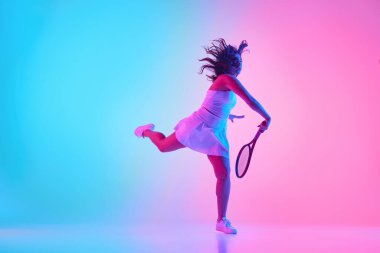 Tenis elbisesi giymiş, raketini neon ışıkta canlı gradyan stüdyo arkaplanına doğru sallamaya hazır bayan sporcunun dinamik görüntüsü. Profesyonel spor konsepti, şampiyonluk, turnuva. Ad