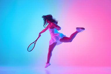 Beyaz kıyafetli bayan tenisçi canlı gradyan stüdyo arka planına karşı neon ışıkta güçlü bir atış yapmak için sıçrıyor. Profesyonel spor konsepti, şampiyonluk, turnuva. Ad