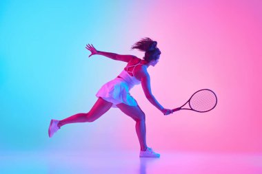 Beyazlı bayan tenisçinin yan görünüşü, canlı gradyan stüdyo arka planına karşı neon ışıkta güçlü bir salıncak sergiliyor. Profesyonel spor konsepti, şampiyonluk, aktif yaşam tarzı, turnuva.