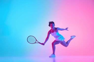 Kadın tenisçi elbisesi, topa neon ışıkta vurmaya hazırlanırken hareketli gradyan stüdyo arkaplanına doğru hamlenin ortasında çekildi. Profesyonel spor konsepti, şampiyonluk, turnuva. Ad