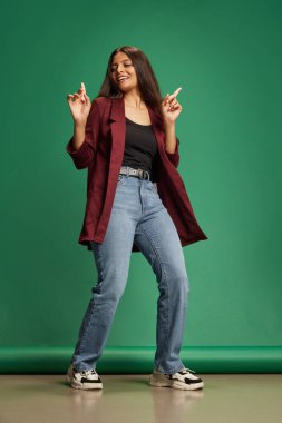 Neşeli genç Hintli kadın gündelik giyinmiş dans ediyor ve yeşil stüdyo geçmişine karşı el kol hareketi yapıyor. Eğlence anlayışı, yaşam tarzı, insan duyguları, hobi, moda ve tarz. Ad