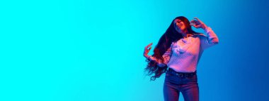 Pankart. Genç bir kadın, neon ışıkta dans eden çekici bir Hintli. Mavi arka planda dans ediyor. Metin eklemek için negatif alanı var. Müzik, moda ve tarz kavramı, dinlenme, dinlenme.