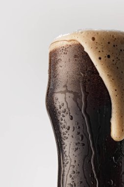 Bardak ağzına kadar koyu birayla dolu, kremalı, bronz köpüklü gri stüdyo arka planına doğru çağlayan köpüklü. Yiyecek ve içecek kavramı, kutlama, Ekim festivali, içecek endüstrisi. Ad