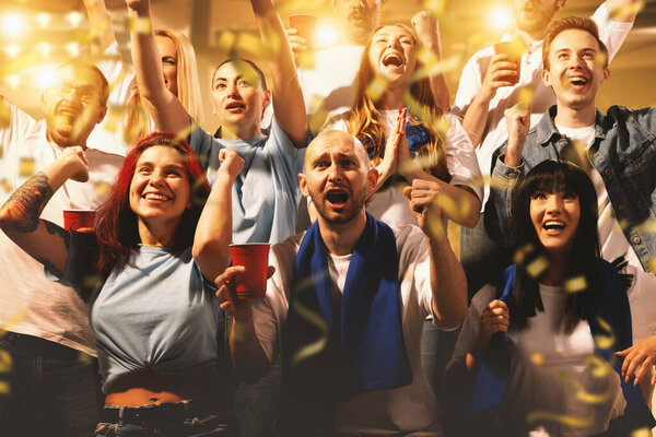 Crowd of sport fans cheering during match on stadium. Excited people standing raised arms , clapping and yelling to encourage their team. Concept of sport, competition, support, world, cup. Ad