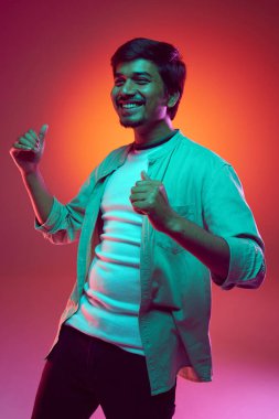 Genç adam neon ışığı altında arka planda dans ederken neşe ve güven anı yaşıyor. Moda ve tarz kavramı, insani duygular, hobi, pozitif.