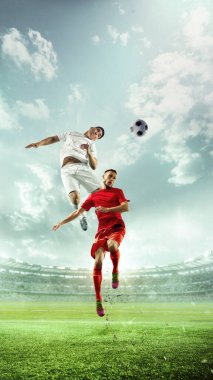 Dinamik, dikey odaklı fotoğraf. Havada kırmızı ve beyaz formalar içinde futbol oyuncuları, tezahüratlı seyircilerle dolu stadyumda top için yarışıyorlar. Spor oyunları, şampiyonluk, turnuva konsepti