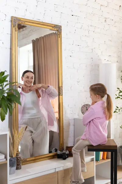 stock image Cute little girl sees her elderly self in mirror, symbolizing journey from childhood innocence to lifetime of experiences. Concept of past and future, generation, memories, female beauty, childhood.