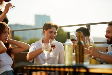 Güneş, kutlamalarda içkilerini kaldıran bir grup genç insanın üzerine altın bir parıltı saçıyor. Parti anlayışı, Cuma havası, kutlama, yaz tatili, rahatlama.