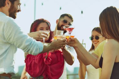 Güneş, güzel zamanlara ve harika arkadaşlara kadeh kaldırırken, kadın ve erkeklerden oluşan bir grubun üzerinde ışıldıyor. Parti anlayışı, Cuma havası, kutlama, yaz tatili, rahatlama.