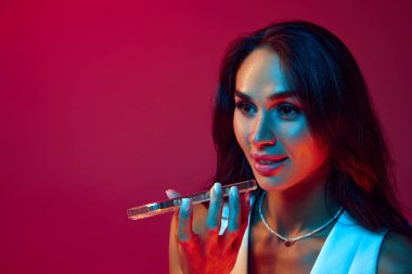 Neşeli genç esmer kadın telefonda konuşuyor, sesini neon renkli akıllı telefonuyla çeviriyor, lacivert stüdyo arka planına karşı, modaya uygun renklere. Teslimat sertifikası, iletişim.