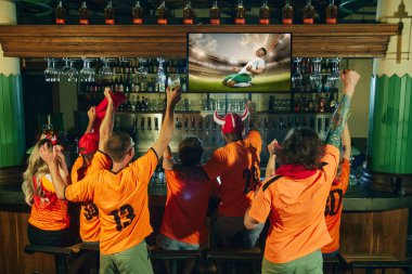 Turuncu gömlekli tutkulu hayranlar barda tezahürat yapıyor, kolları zaferle kalkıyor ve büyük ekranda maç izliyorlar. Arkadaşlık kavramı, futbol fanatiği, şampiyonluk, destek, kutlama. Ad