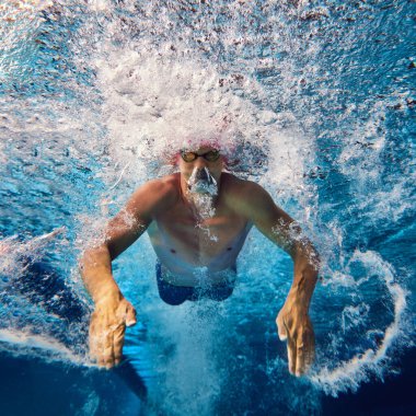 Eğitimde su altında görülen odaklanmış yüzücü, pembe başlık ve gözlük takıyor, güçlü vuruşları dinamik su hareketi yaratıyor. Profesyonel spor anlayışı, hareket. Su altı çekimi..
