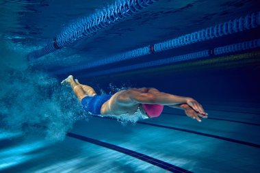 Dalış ortasında erkek yüzücü, güçlü bir form ve hassasiyet gösteriyor. Antrenman sırasında suyu kesiyor. Profesyonel spor kavramı, rekabet, hareket. Su altı çekimi..